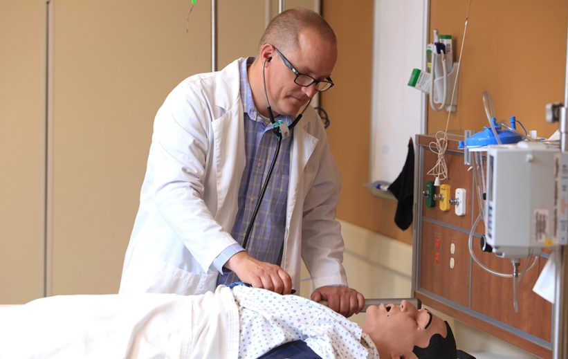 A nurse in a white coat practices in Alverno's nursing simulation center.