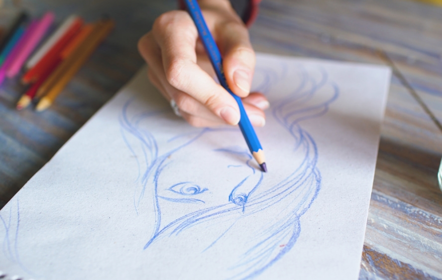 An artist sketches a woman on a white piece of paper with a blue colored pencil