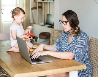 Woman working on laptop while watching her child