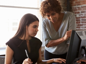 A professional businesswoman shows a business student a process on a desktop computer