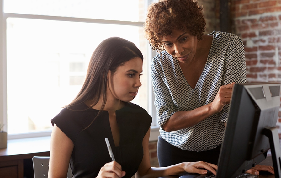 A professional businesswoman shows a business student a process on a desktop computer