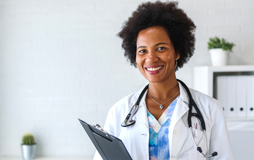 A nurse in a white coat holding a clipboard smiles