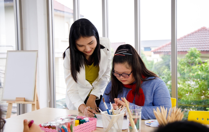 A young art teacher helps a special needs student with a project